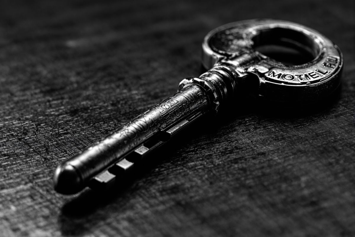 Llave de habitación de latón con llavero de peso sobre el mostrador pulido
            de recepción, con luz rasante marcando el metal gastado.